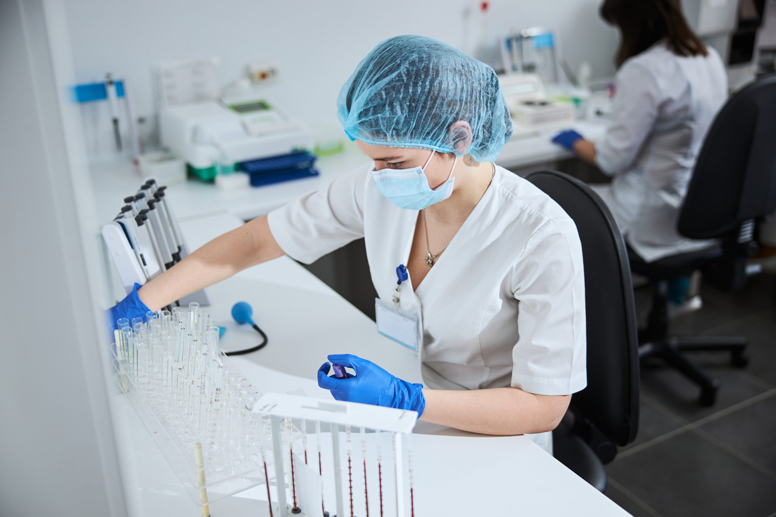 Focused serious young Caucasian female lab technician holding a glass vial with a screw cap